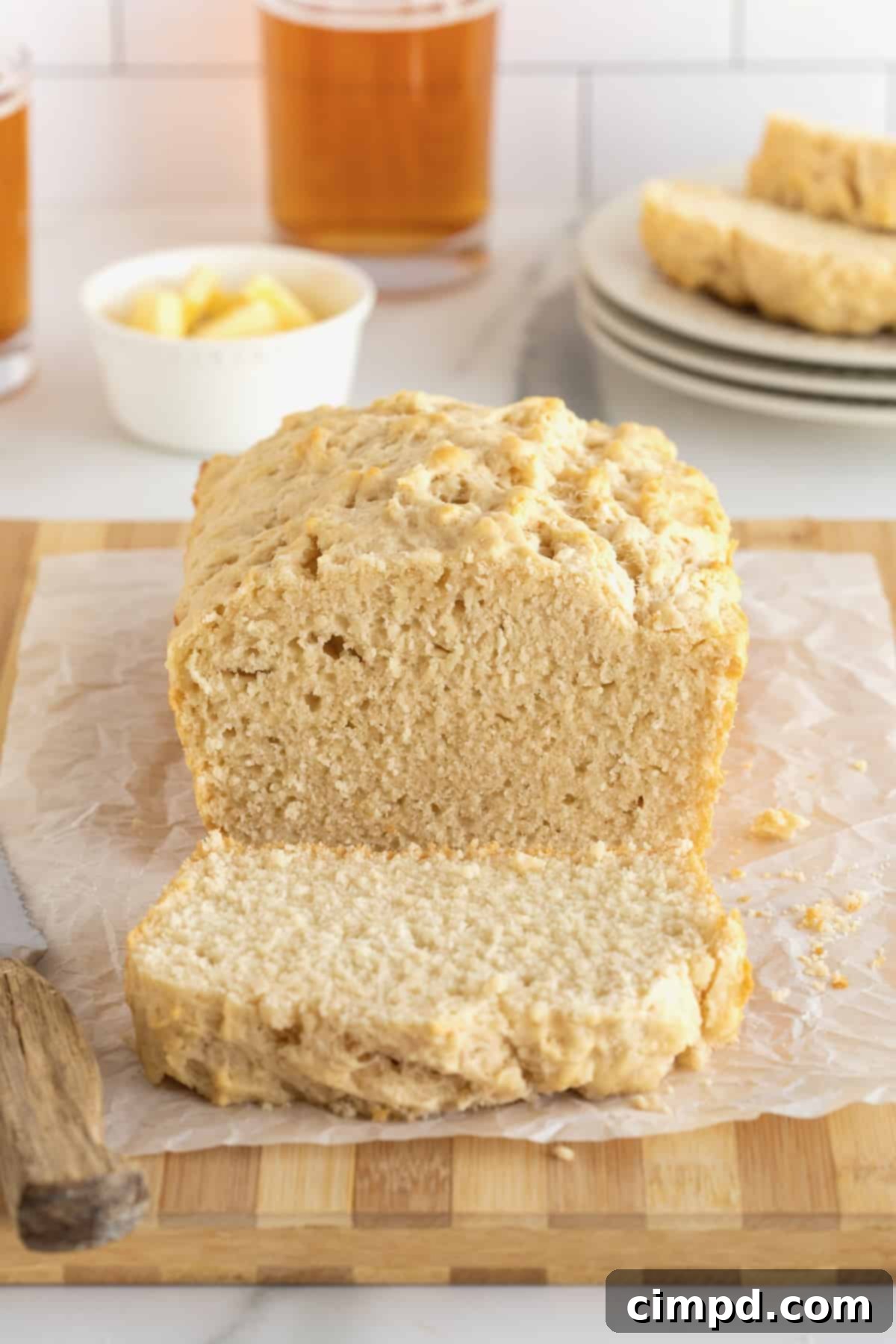 Pub-Style Beer Bread 2 A golden-brown loaf of beer bread sliced on a wooden cutting board, with a small dish of melted butter in the background.