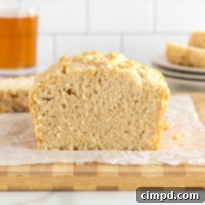 Pub-Style Beer Bread 14 A golden-brown loaf of beer bread sliced on a wooden cutting board with a small dish of melted butter in the background.