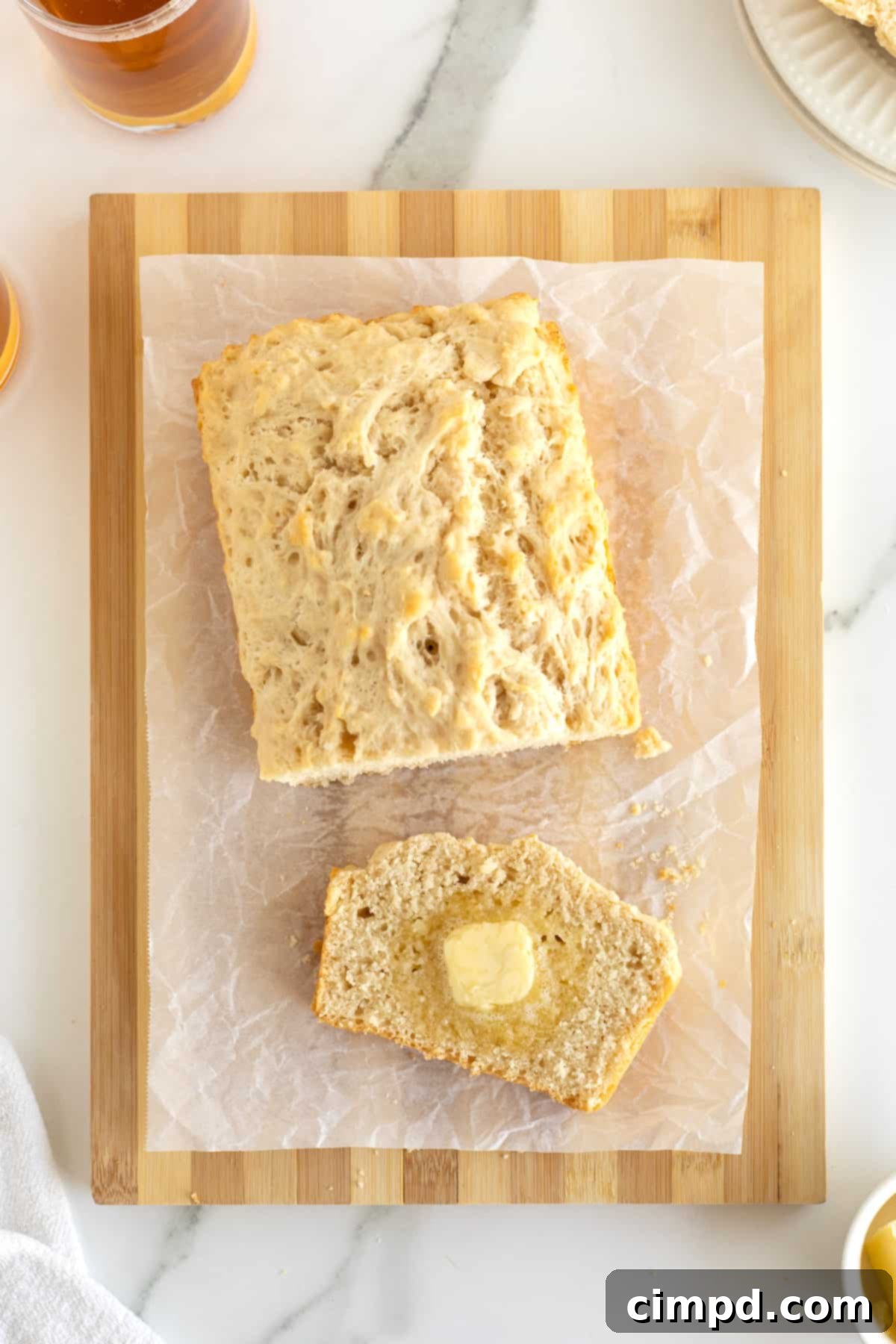 Pub-Style Beer Bread 3 A whole loaf and a single slice of beer bread on a parchment-lined wooden cutting board, ready to be enjoyed.