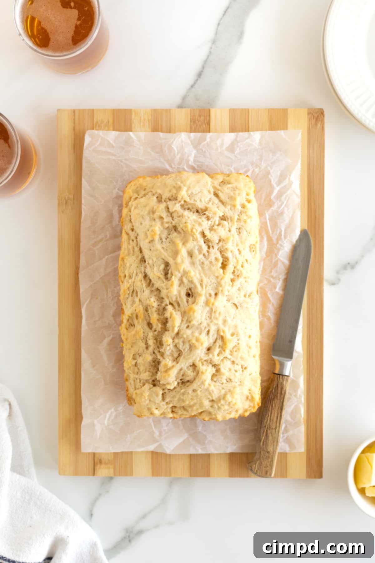 Pub-Style Beer Bread 5 A freshly baked loaf of beer bread sitting beside a bread knife on a parchment-lined wooden cutting board.