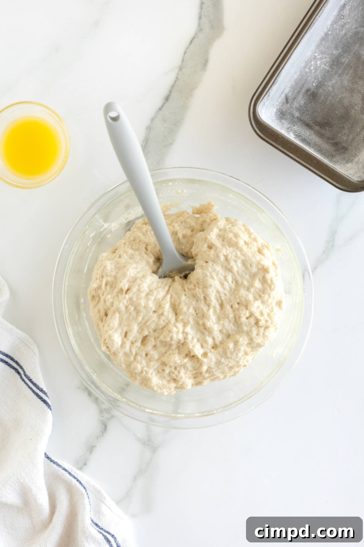 Pub-Style Beer Bread 9 A glass bowl containing lumpy beer bread dough, with a rubber spatula resting inside, illustrating the ideal consistency before baking.