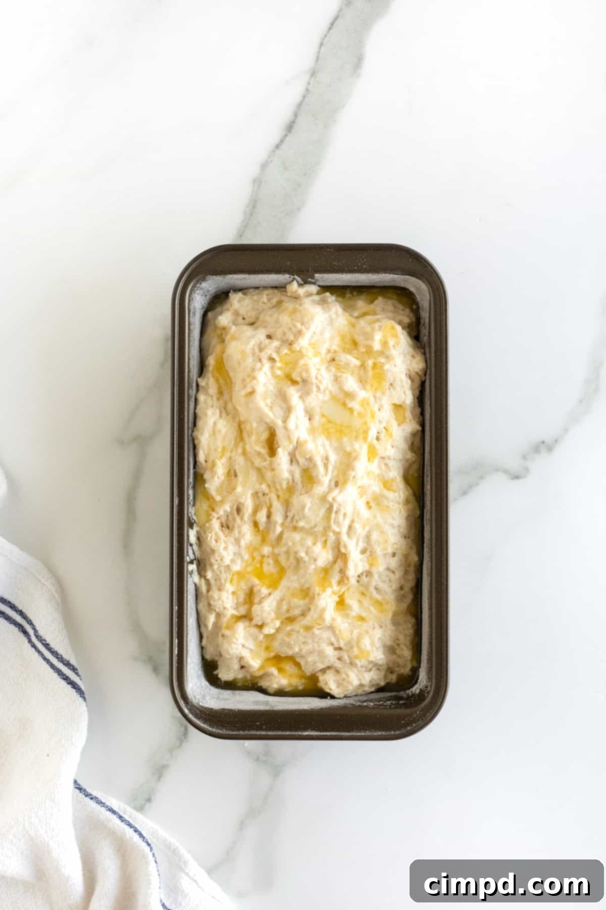 Pub-Style Beer Bread 10 Beer bread dough poured into a floured dark metal loaf pan, ready for the oven, resting on a clean white marble counter.