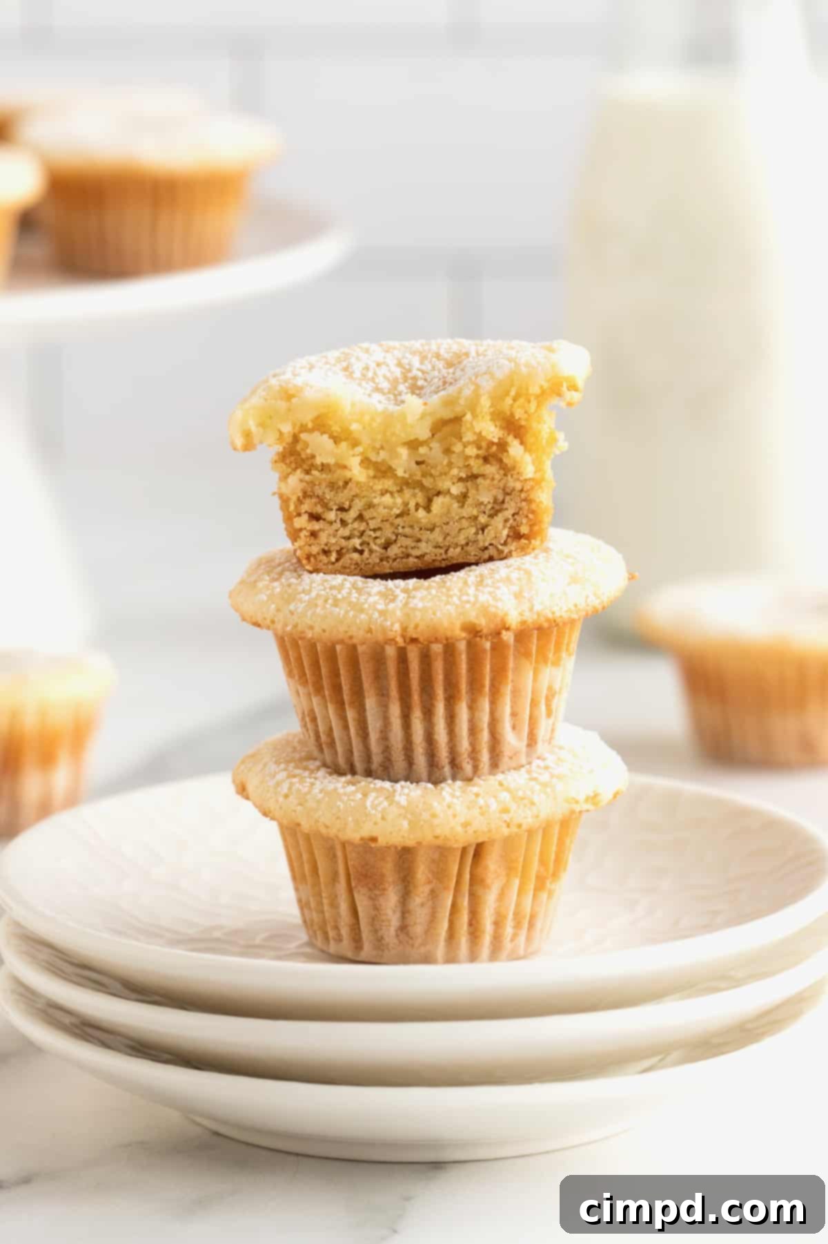 Chewy Butter Cake Squares 3 Three golden-brown two-bite butter cake bites, delicately sprinkled with powdered sugar, elegantly presented on a stack of three pristine white plates, highlighting their inviting texture.
