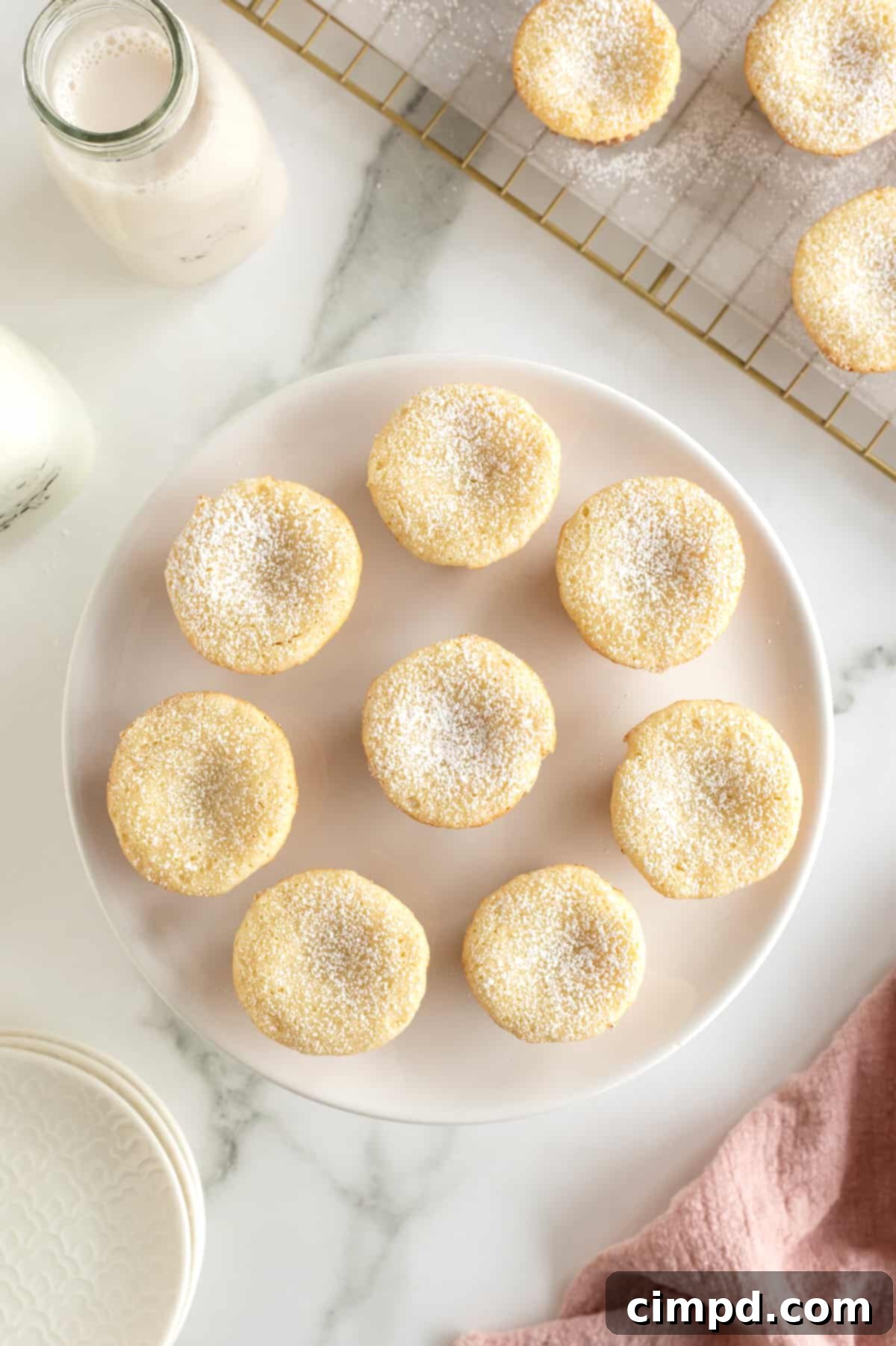 Chewy Butter Cake Squares 4 A pristine white serving plate showcases eight beautifully arranged two-bite gooey butter cakes, each generously sprinkled with powdered sugar, inviting you to take a bite.