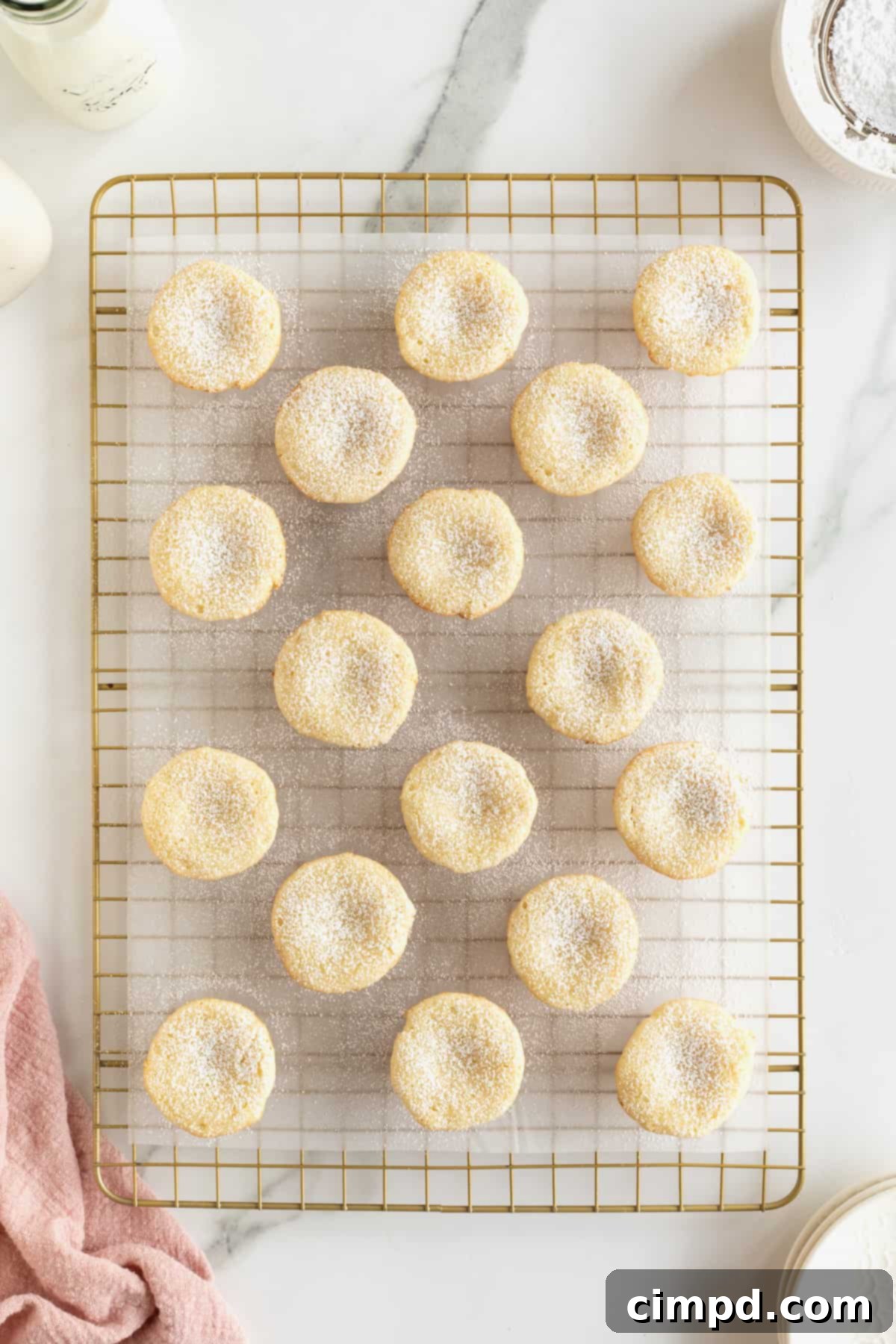 Chewy Butter Cake Squares 9 A parchment-lined cooling rack filled with freshly baked mini gooey butter cakes, each delicately sprinkled with powdered sugar, creating an enticing visual display.