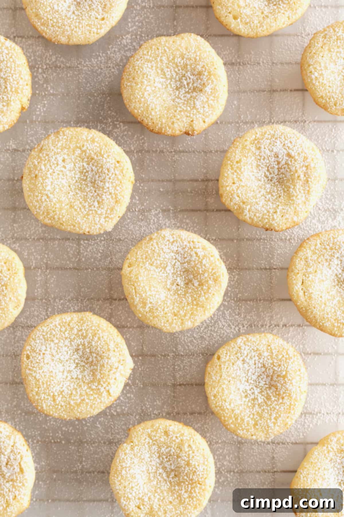 Chewy Butter Cake Squares 10 A parchment-lined cooling rack filled with mini gooey butter cakes, freshly baked and generously sprinkled with powdered sugar, ready for cooling and serving.