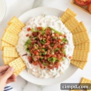 Ultimate BLT Dip 12 A white serving bowl with a creamy white dip topped with crumbled bacon and shredded lettuce with club crackers on the side.