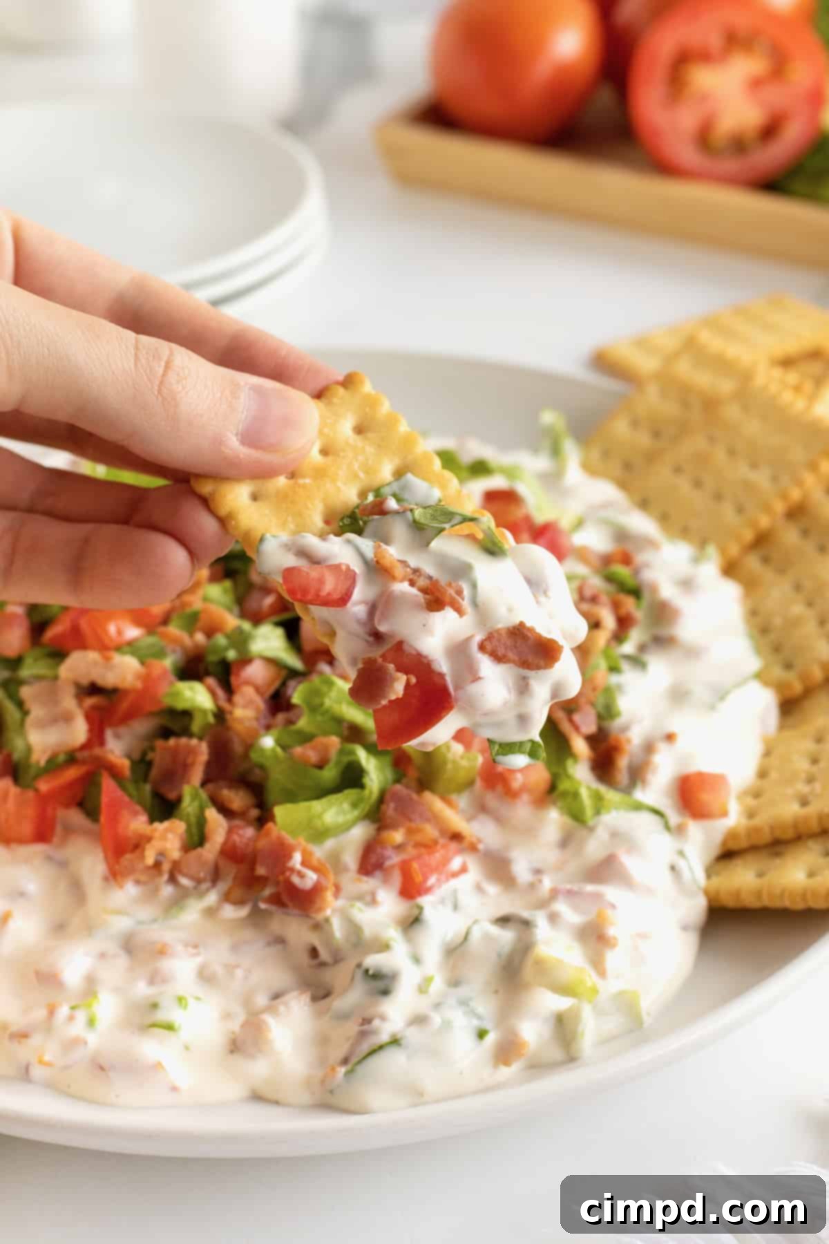 Ultimate BLT Dip 4 An overhead view of the creamy BLT Dip, artfully arranged in a rustic white serving bowl, topped with crispy bacon bits, fresh green lettuce, and diced tomatoes, ready to be served with crackers.