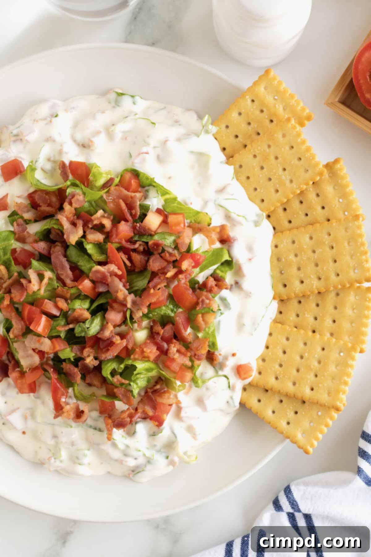 Ultimate BLT Dip 5 A spoonful of creamy BLT Dip being scooped from a white serving bowl, showcasing its rich texture and the delightful mix of bacon, lettuce, and tomato, with crackers nearby.