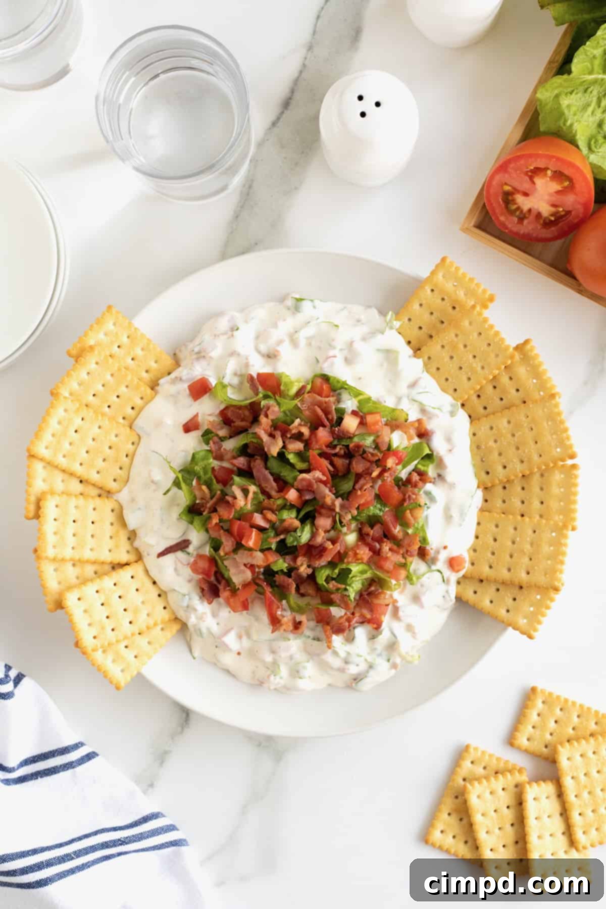Ultimate BLT Dip 9 A white ceramic bowl filled with creamy BLT Dip, generously topped with crumbled crispy bacon and fresh shredded lettuce, accompanied by a scattering of golden club crackers.