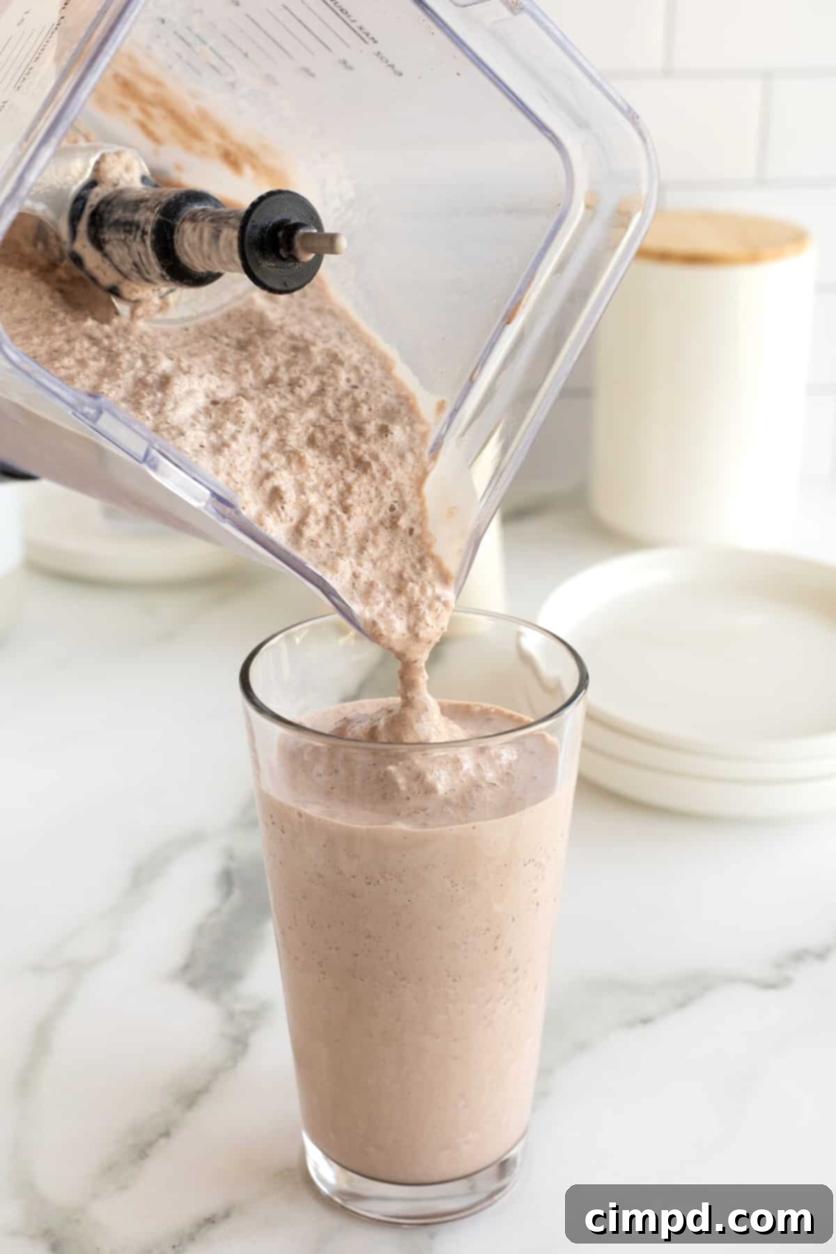 A blender pouring a homemade Wendy's frosty into a tall clear glass, showing its thick and creamy texture.
