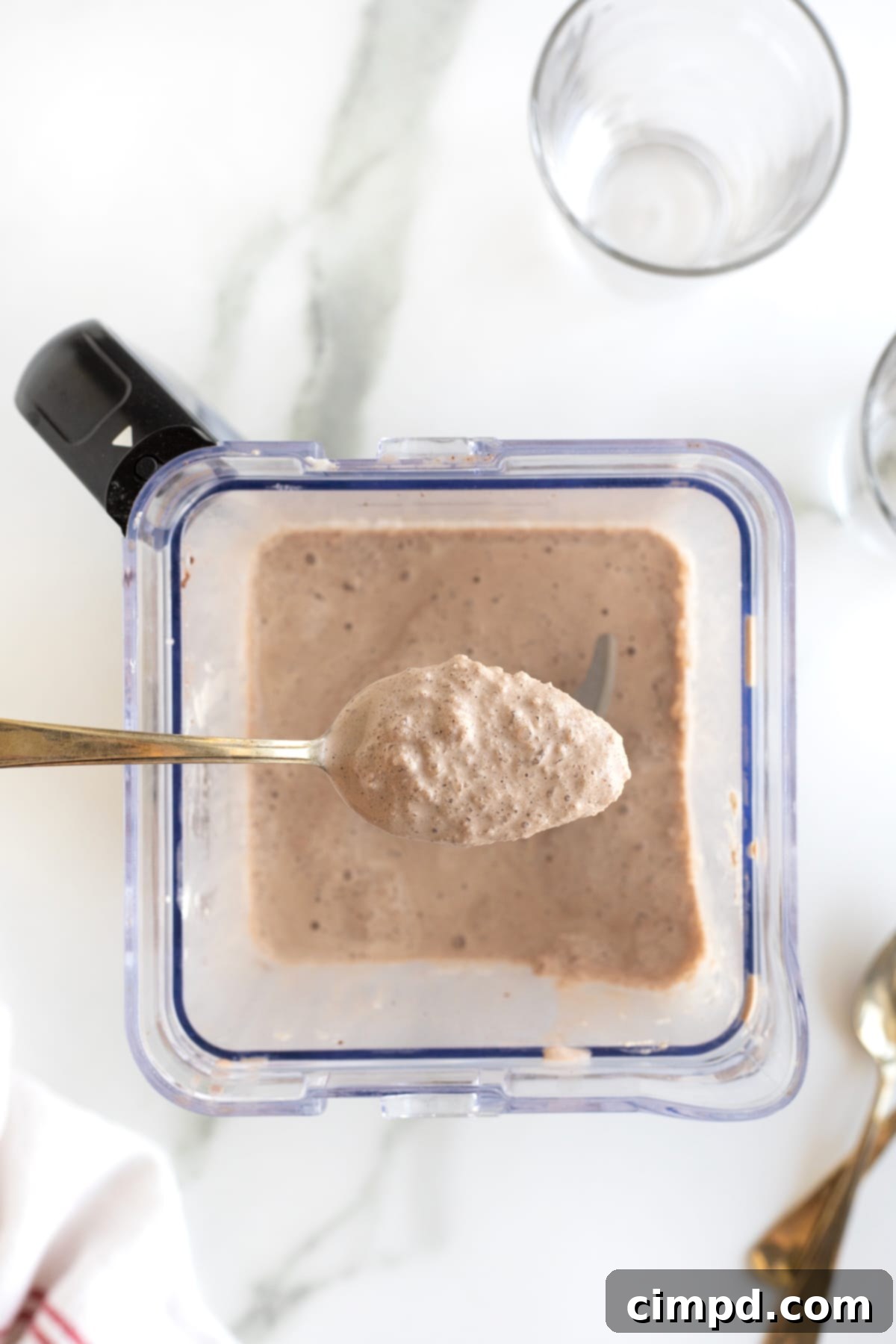 A homemade Wendy's Frosty in a blender, with a spoon held up, demonstrating the thick, creamy, and perfectly textured consistency with tiny ice crystals.