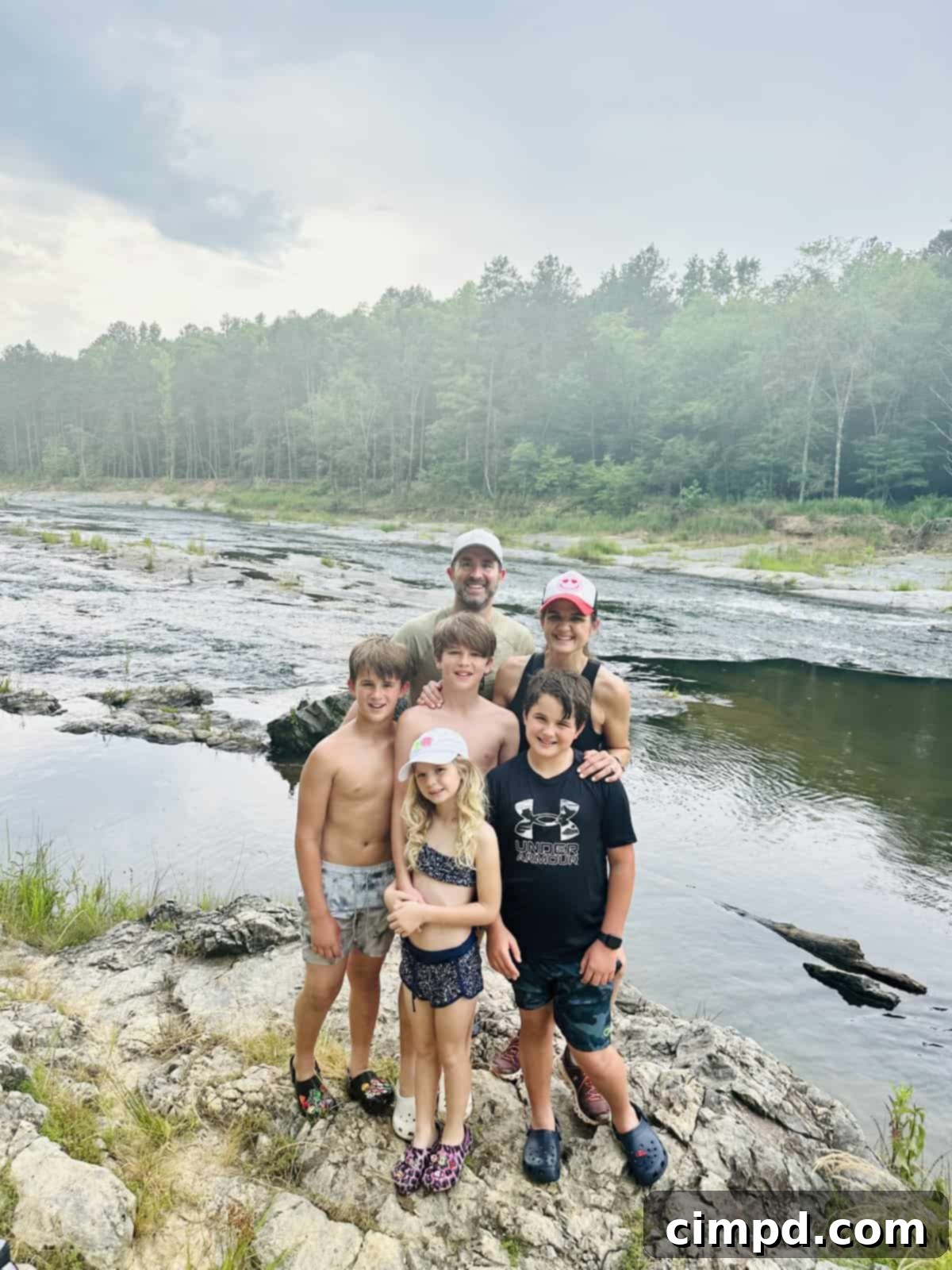 The Brown Family posing happily by a scenic river in Broken Bow, Oklahoma, enjoying their family vacation.