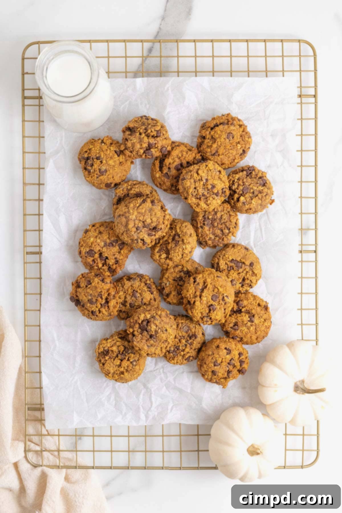 A pile of pumpkin oatmeal cookies on a parchment lined cooling rack.