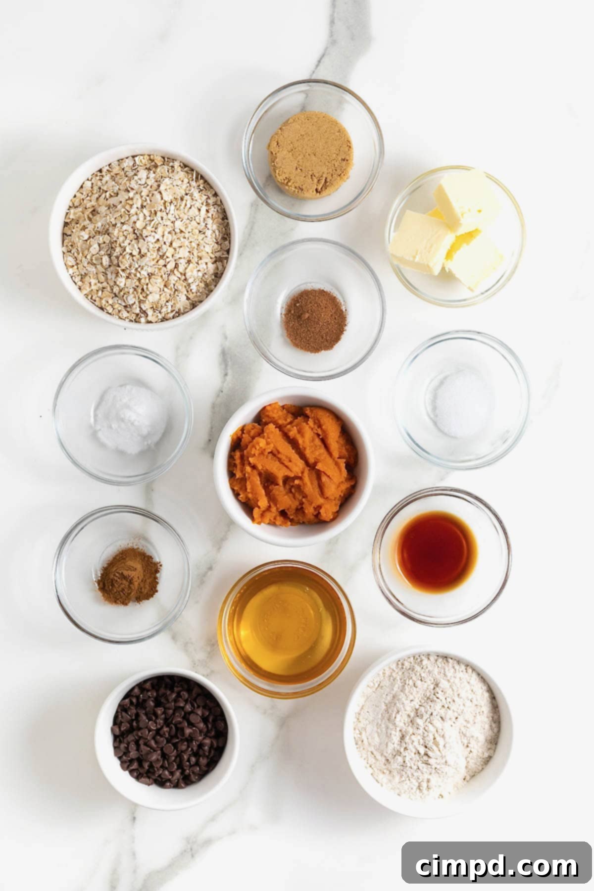 Ingredients to make pumpkin oatmeal chocolate chip cookies in small glass dishes on a white marble counter.
