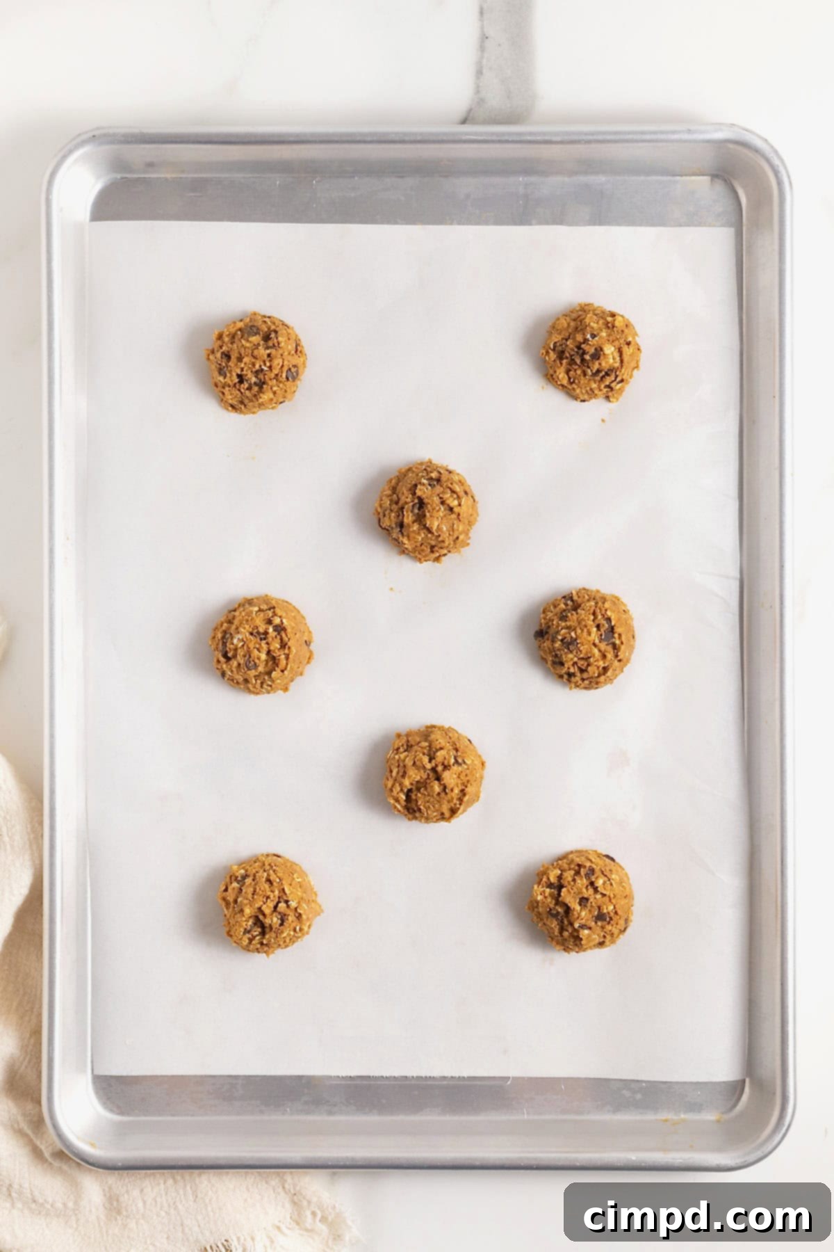 Nine balls of pumpkin oatmeal chocolate chip cookie dough on a parchment lined aluminum cookie sheet.