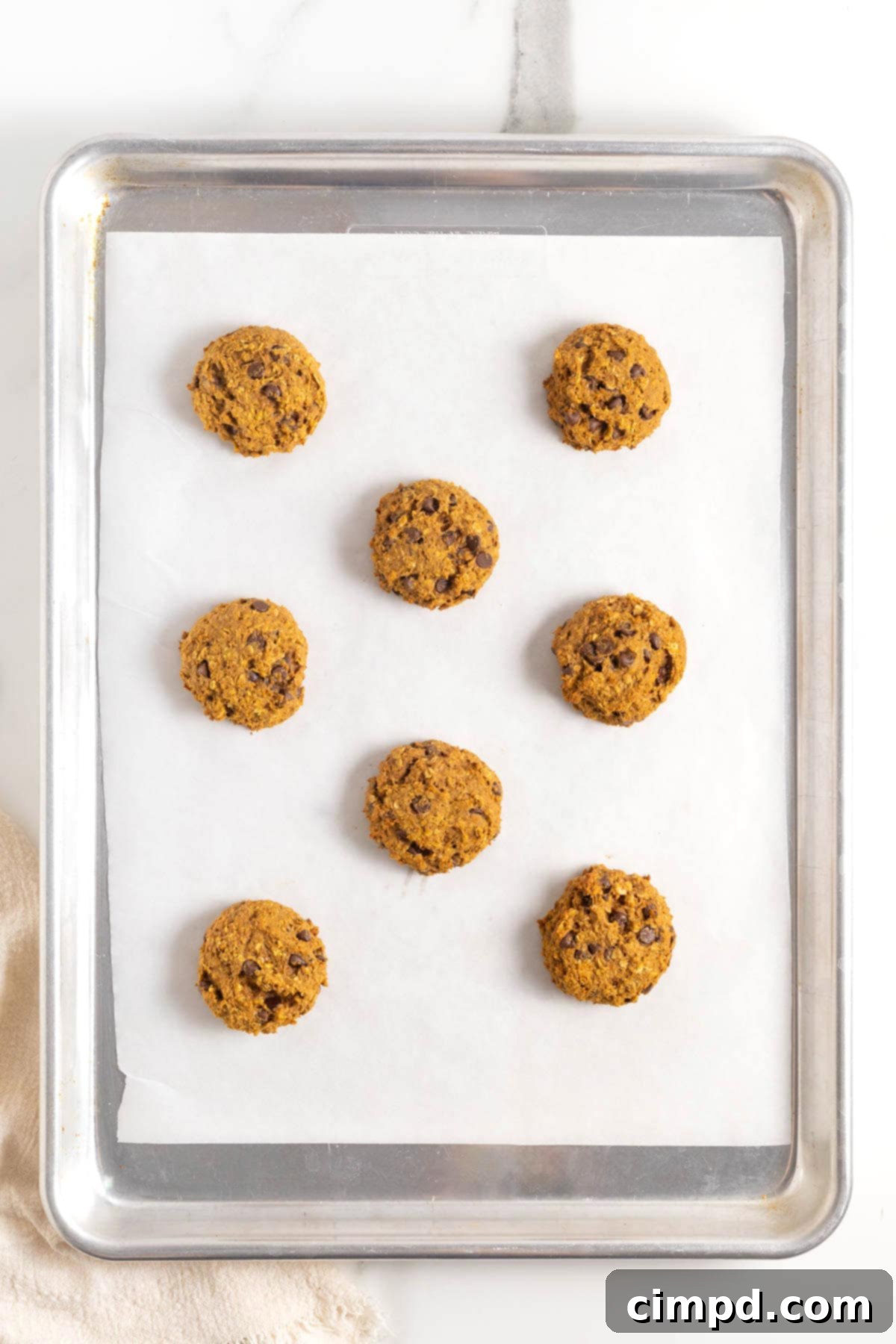 Eight mini pumpkin oatmeal chocolate chip cookies on a parchment lined aluminum baking sheet.