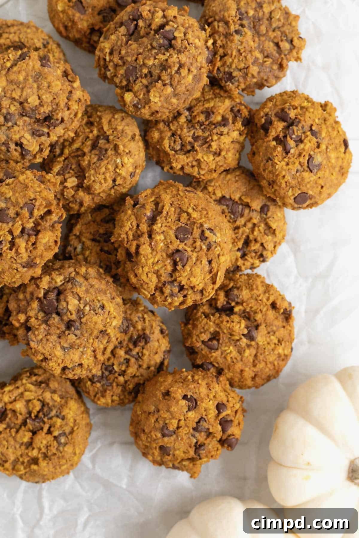 A pile of mini chocolate chip pumpkin oatmeal cookies on a white surface.