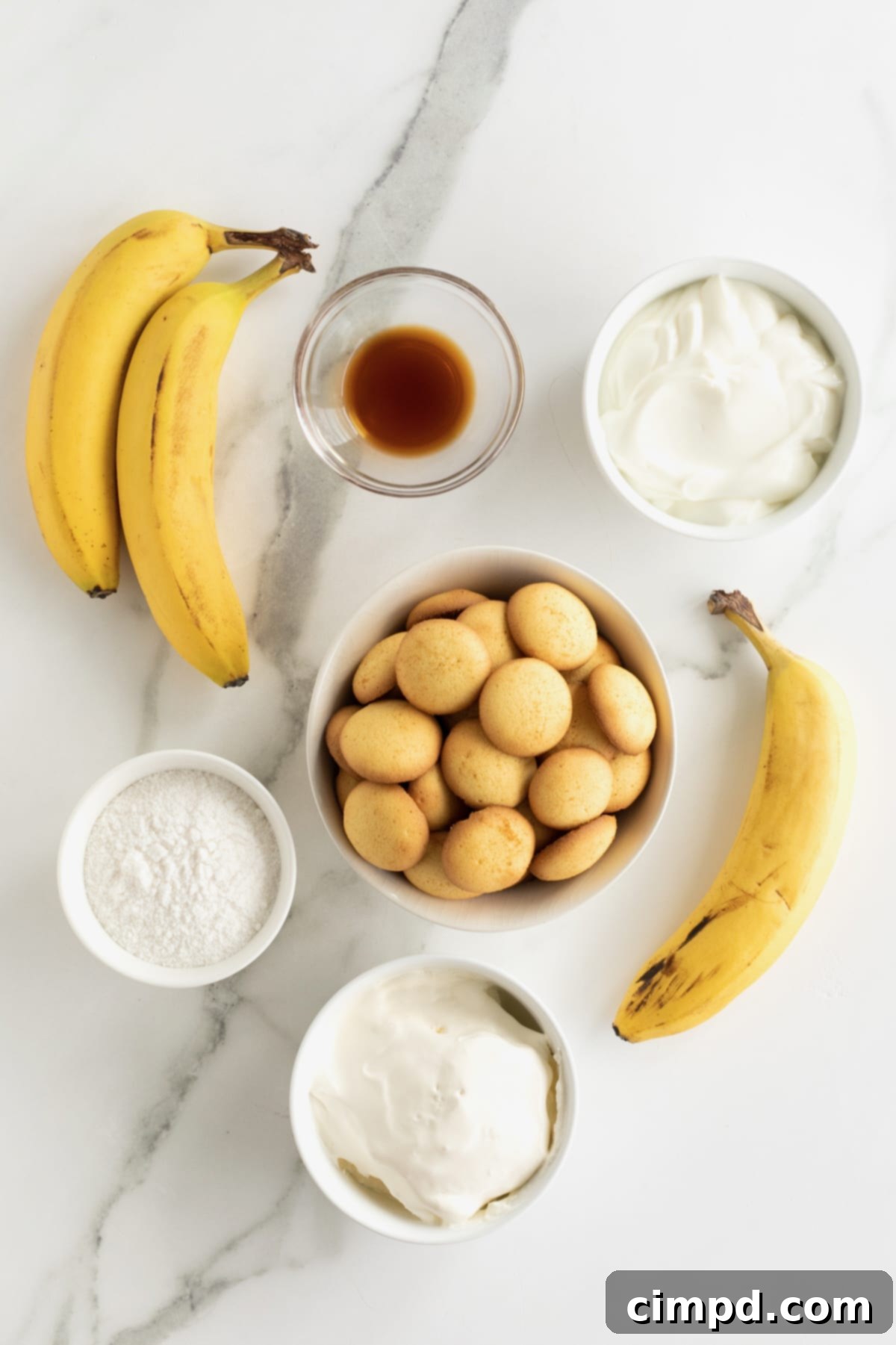 Dreamy Banana Pudding Dip 5 Three ripe bananas, a bowl of Nilla Wafers and small bowls of sour cream, Cool Whip, powdered sugar and vanilla on a white marble counter.