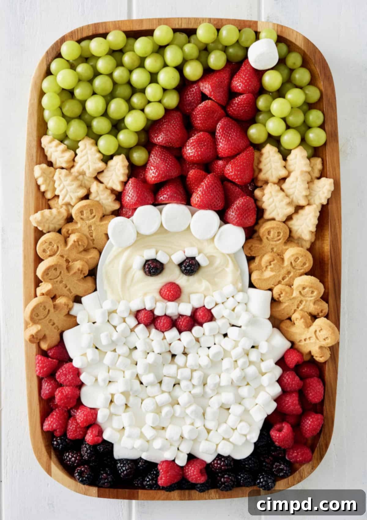 A festive Santa Sweets Board featuring a jolly Santa face made from fruit and marshmallows, surrounded by holiday cookies and green grapes.