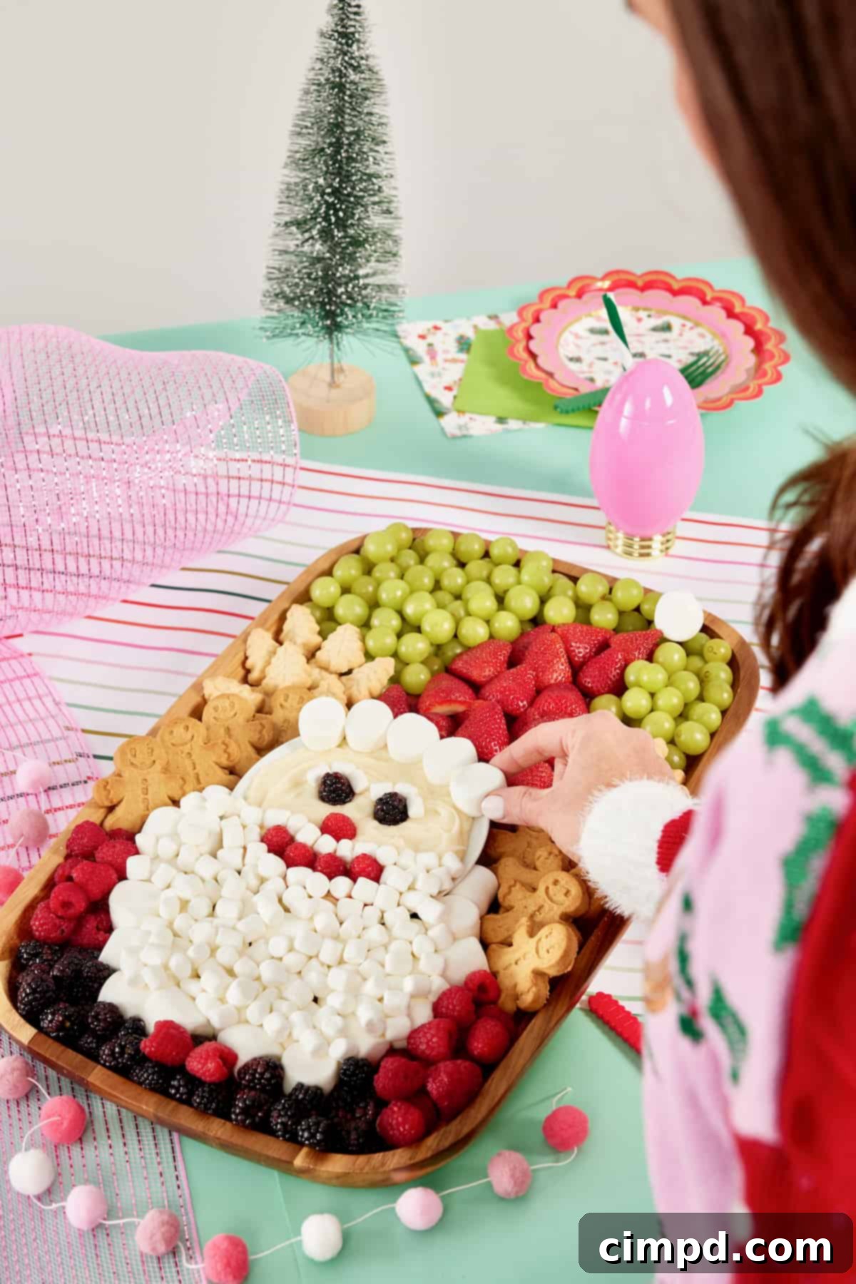 A beautifully composed wood food board, intricately decorated with fresh fruit, delicious cookies, and soft marshmallows to artistically depict Santa Claus's face.