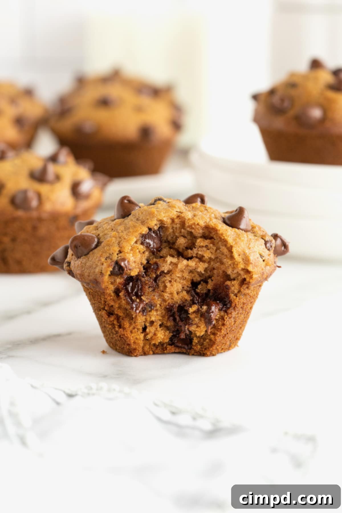 A pumpkin chocolate chip muffin with a bite taken out of it on a white marble counter, showcasing its moist interior and chocolate chips.