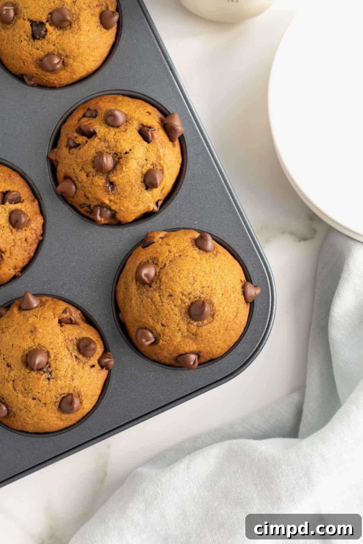 Four pumpkin chocolate chip muffins perfectly baked and cooling in a nonstick muffin pan.