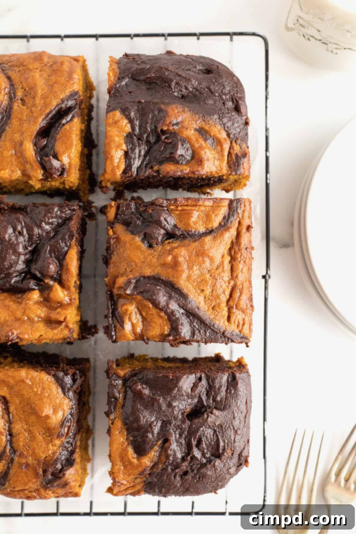 A metal cooling rack with a sheet of parchment covering it with six pumpkin swirled brownies on it.