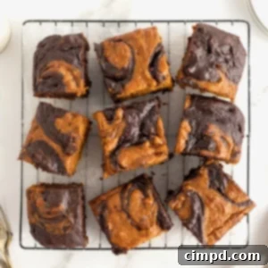 Nine pumpkin swirled brownies on a parchment lined metal cooling rack.