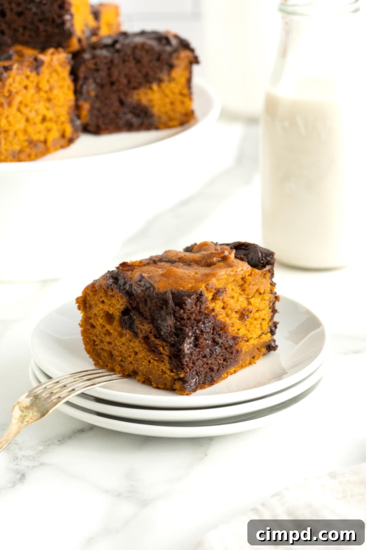A pumpkin swirl brownie on a stack of 3 small white plates accompanied by a fork. A glass of milk sits in the background.