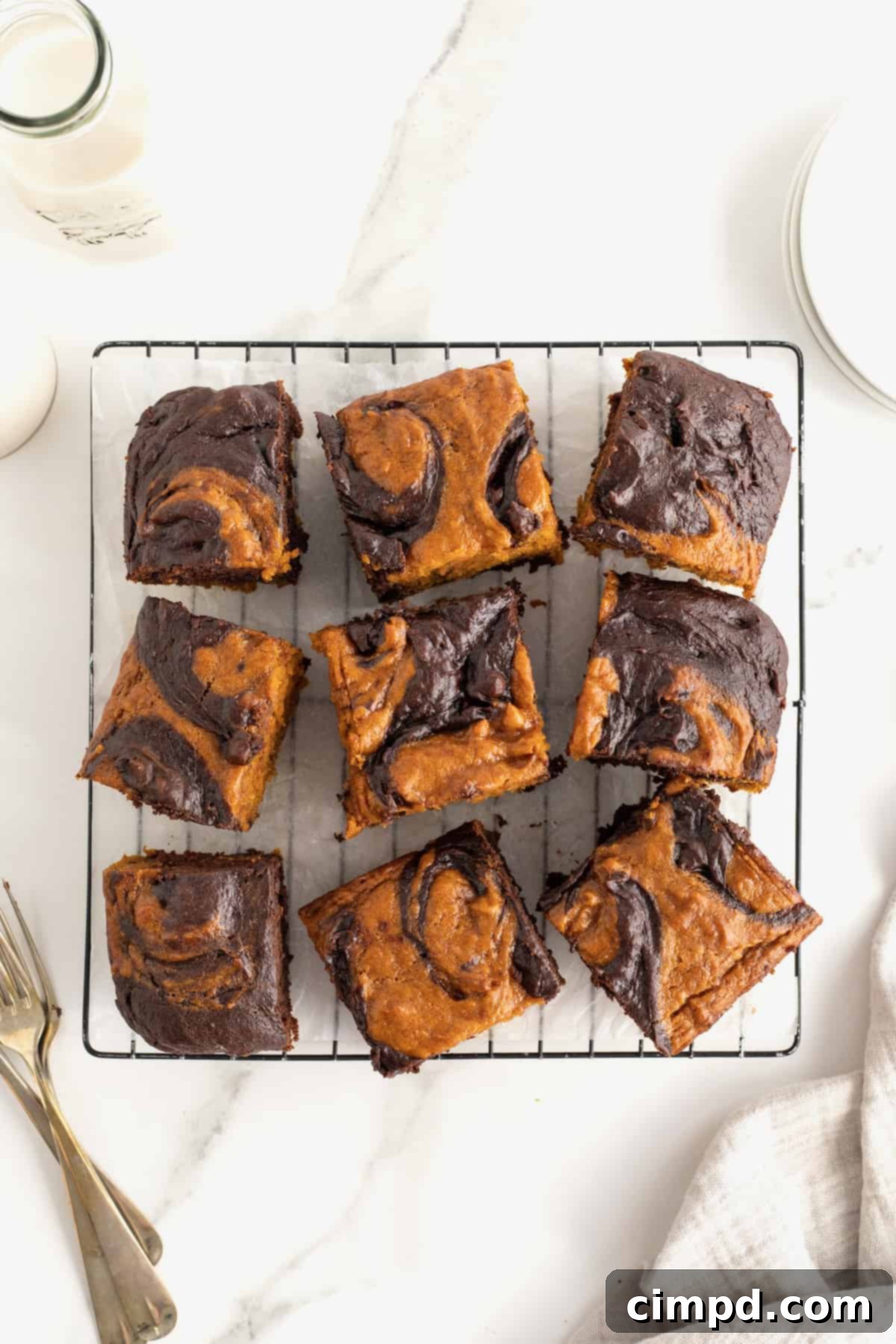 Nine pumpkin swirled brownies on a parchment lined metal cooling rack. 