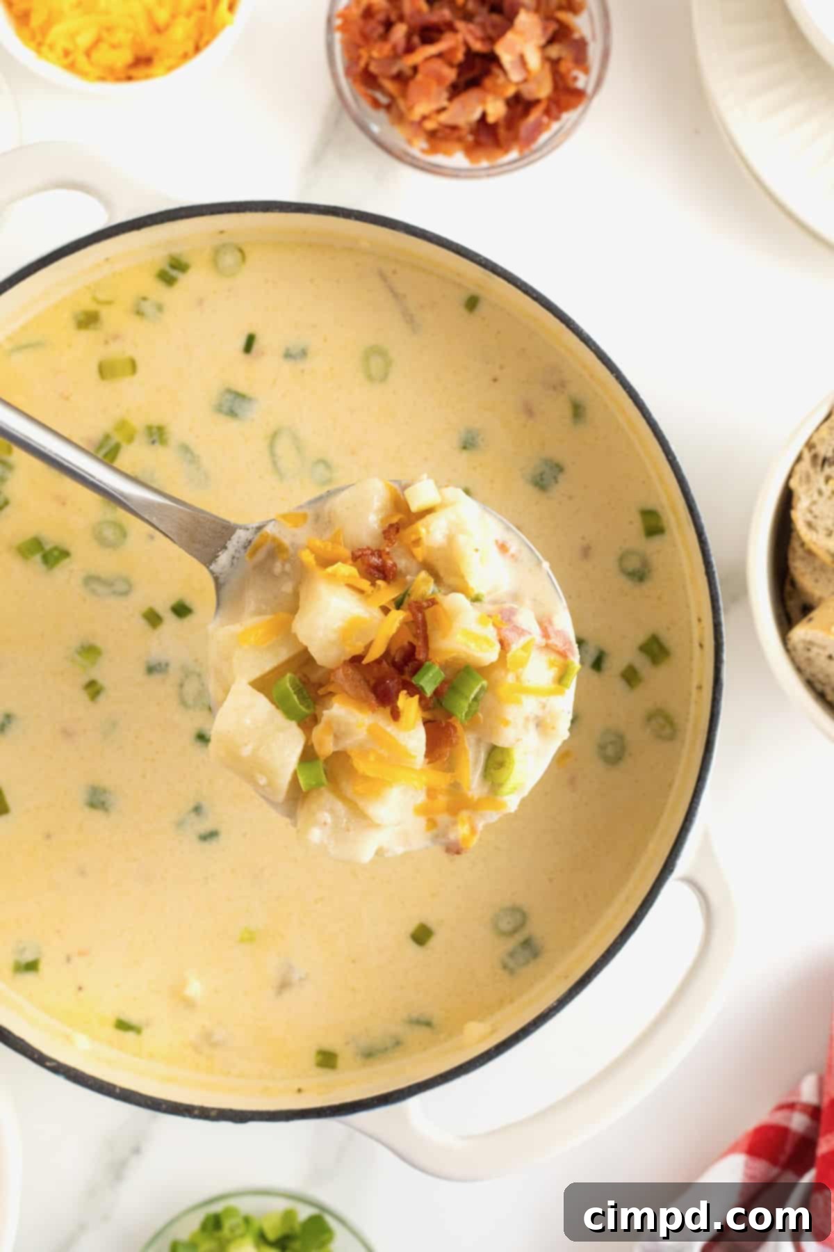 Hearty Loaded Baked Potato Soup 3 A silver ladle overflowing with creamy baked potato soup, suspended over a large white enamel-coated cast iron pot filled with more soup, ready to be served.