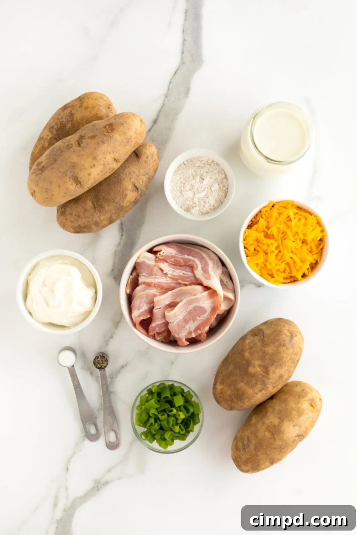 Hearty Loaded Baked Potato Soup 5 A curated display of fresh ingredients for loaded baked potato soup, including russet potatoes, slices of raw bacon, a bowl of flour, milk, shredded cheddar cheese, a dollop of sour cream, and fresh green onions, all arranged on a pristine white marble countertop.