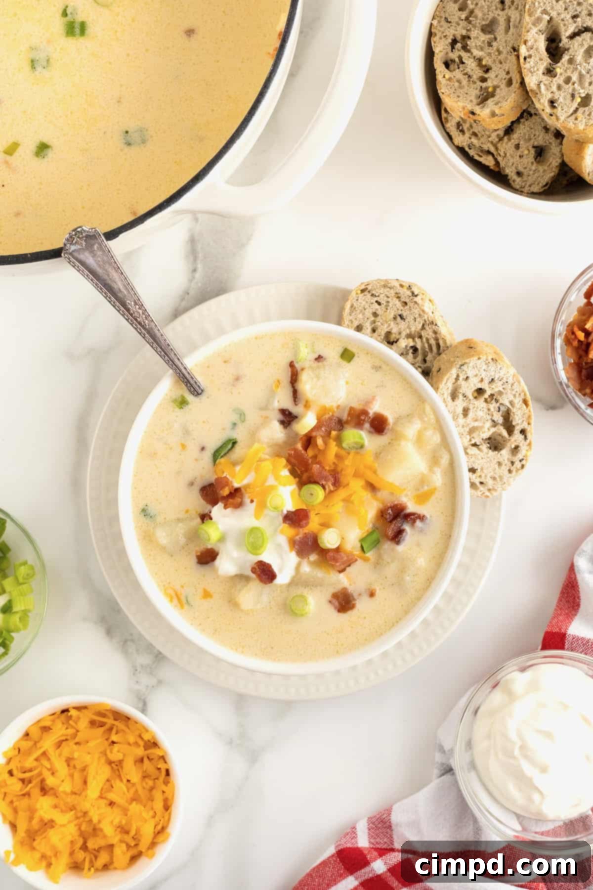 Hearty Loaded Baked Potato Soup 9 A inviting bowl of creamy baked potato soup, exquisitely topped with golden-crisp bacon bits, a generous sprinkle of shredded cheddar cheese, a dollop of cool sour cream, and a scattering of fresh green onions, presented in a clean white bowl.