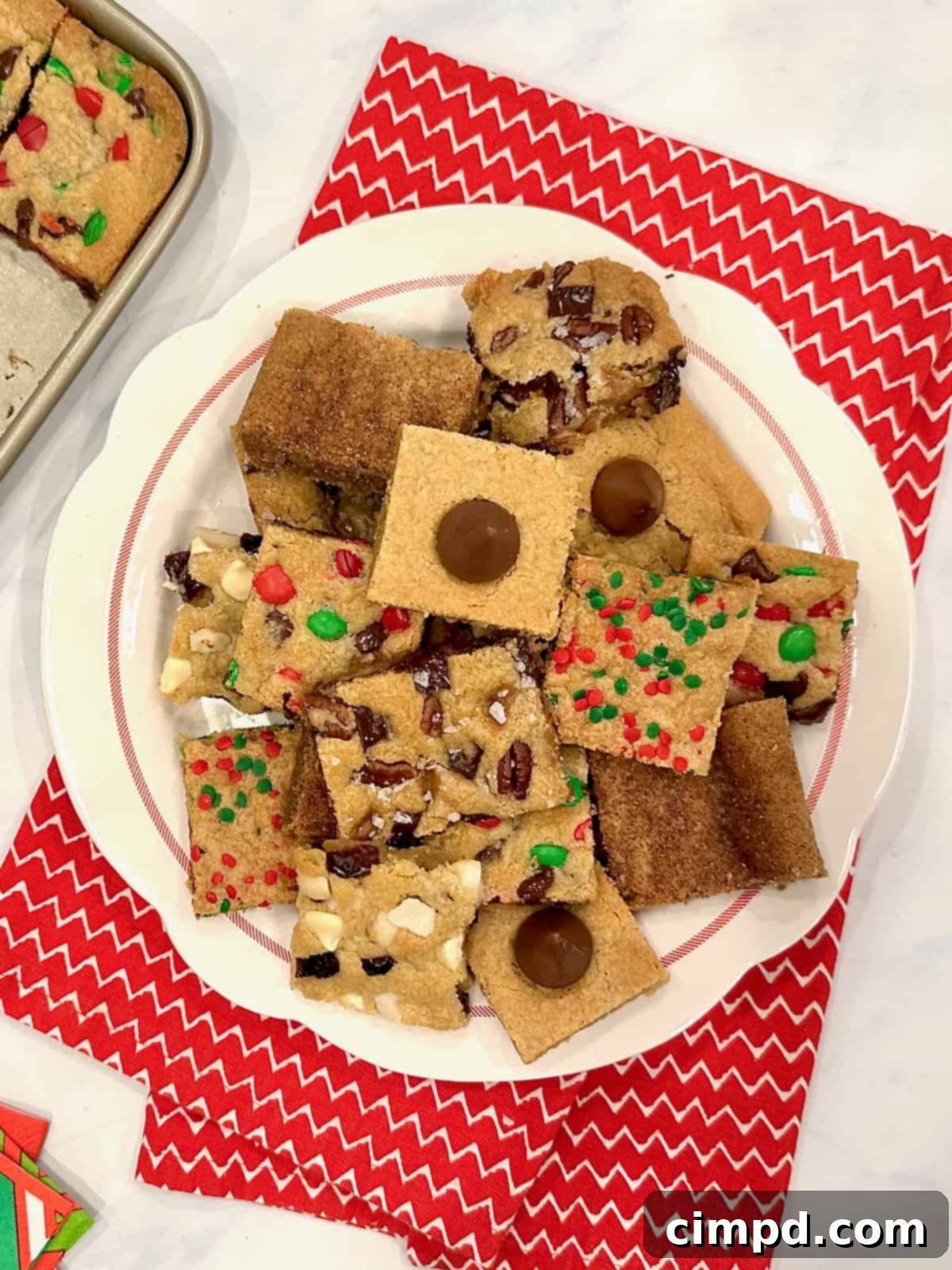 A festive white plate filled with an assortment of holiday cookie bars, artfully placed on a cozy red and white holiday tea towel.