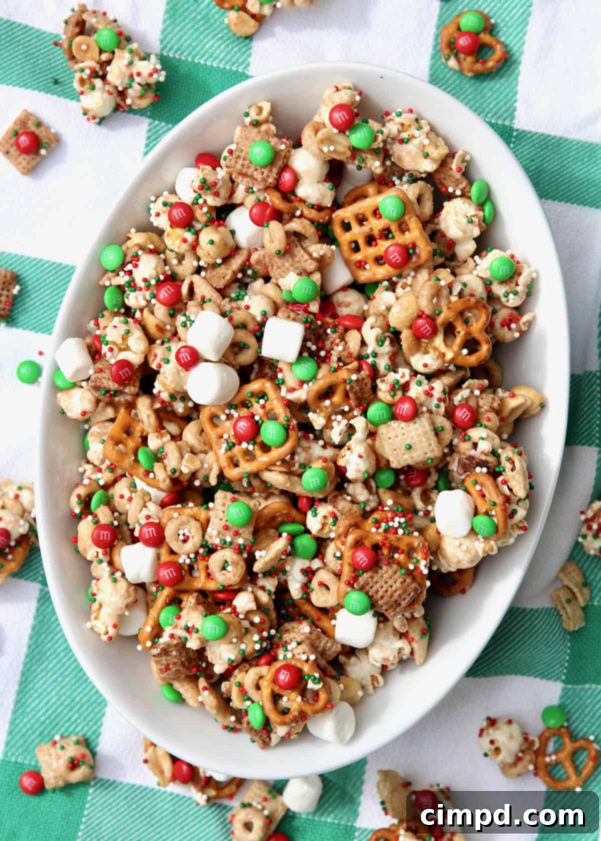 An oval shaped white bowl filled with Christmas party snack mix, glistening with a sweet coating and vibrant colors.