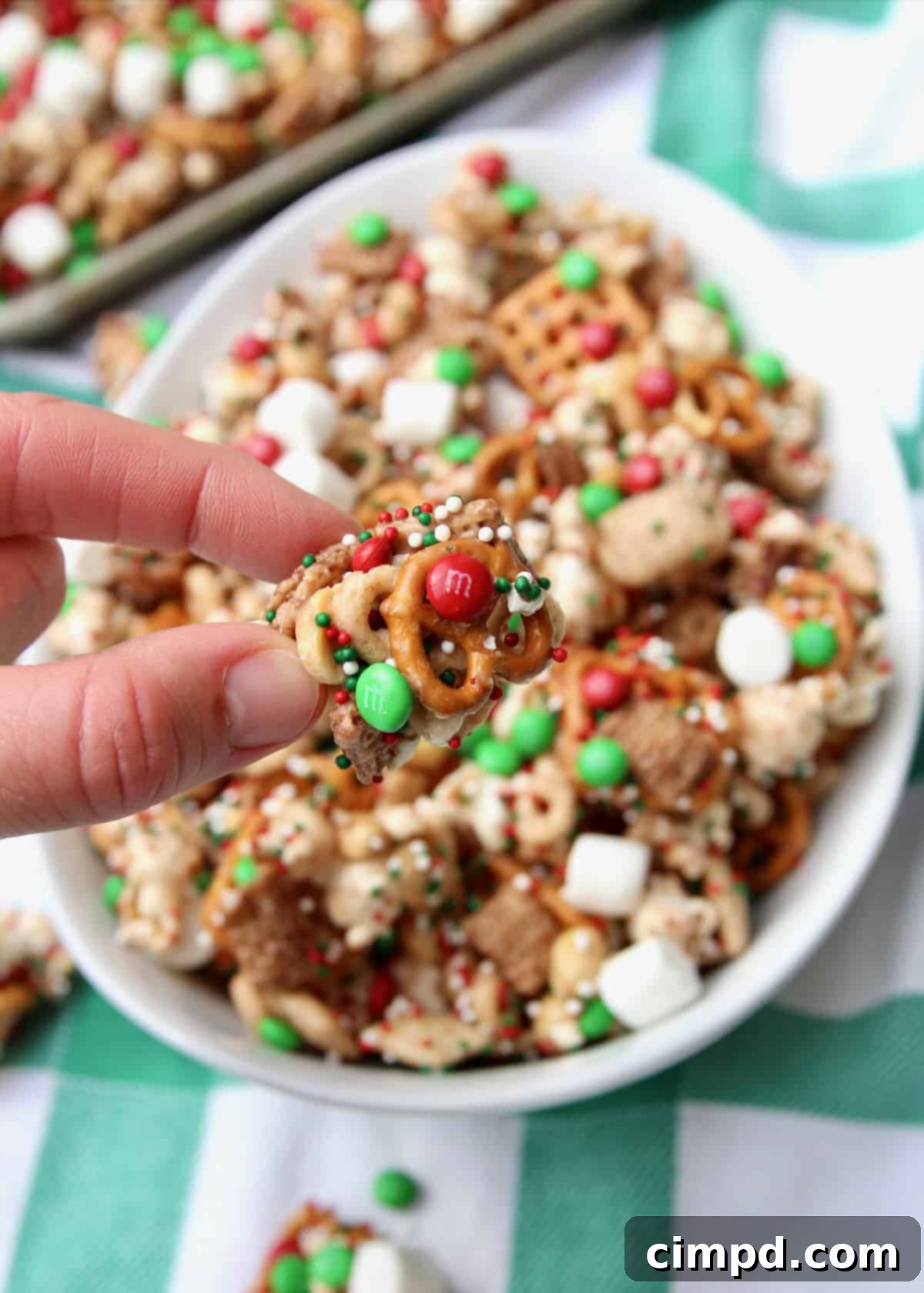An oval shaped white bowl generously filled with a vibrant Christmas party snack mix, highlighting its diverse ingredients and tempting textures.