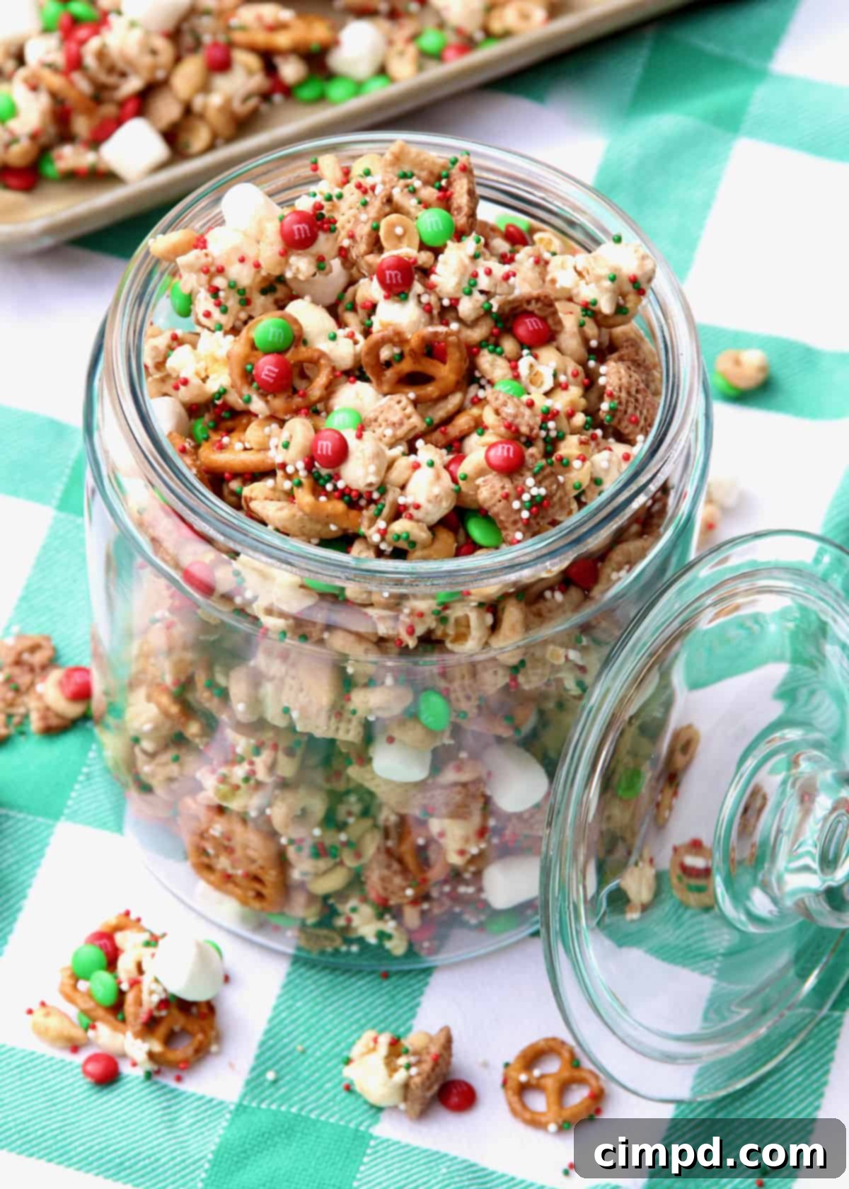 A jar of holiday party snack mix placed on a festive green and white gingham table cloth, evoking a warm and cozy holiday atmosphere.