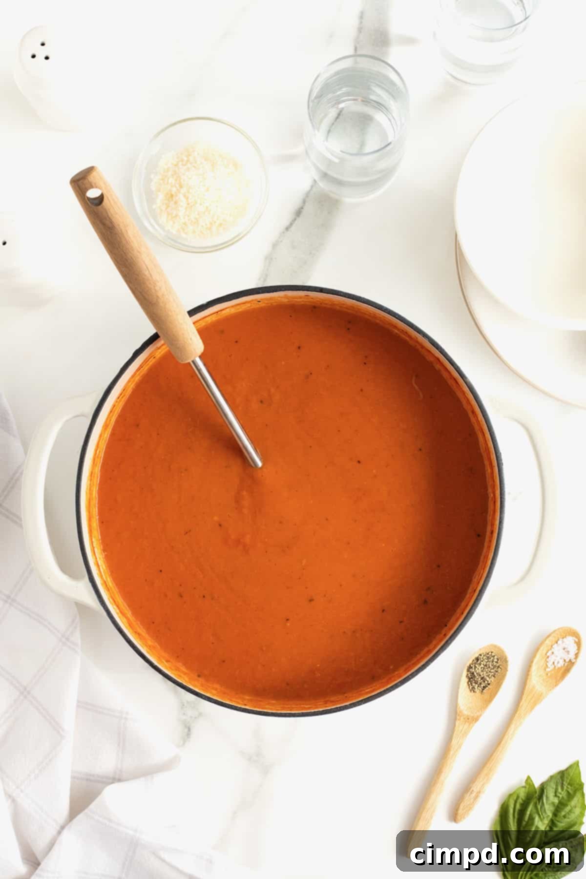A large pot of perfectly cooked creamy tomato soup, with a wooden ladle's handle extending out, ready to serve.
