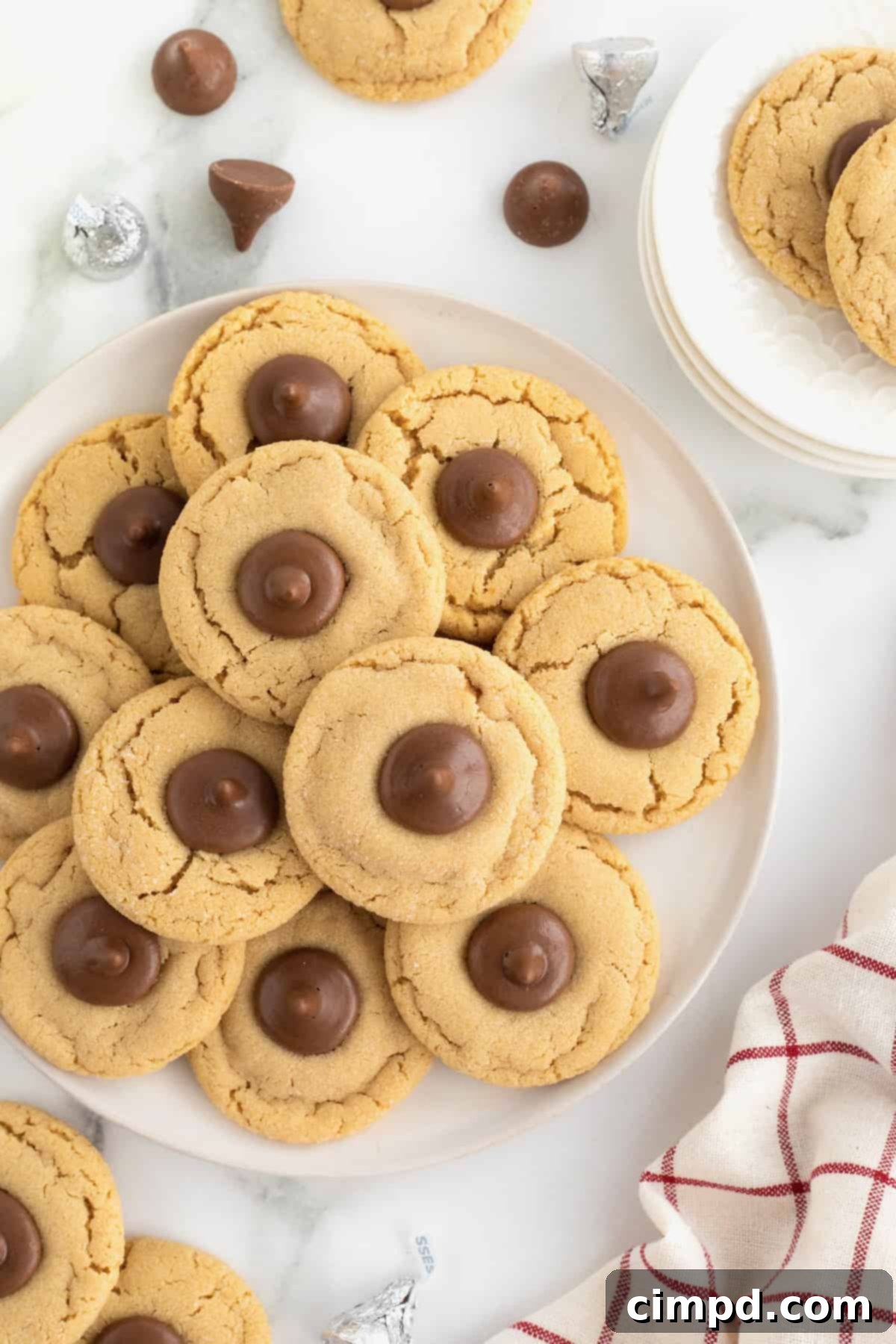 A pile of peanut butter holiday cookies with a Hershey's kiss in the center on a round white serving plate.