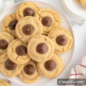 A pile of peanut butter holiday cookies with a Hershey's kiss in the center on a round white serving plate.