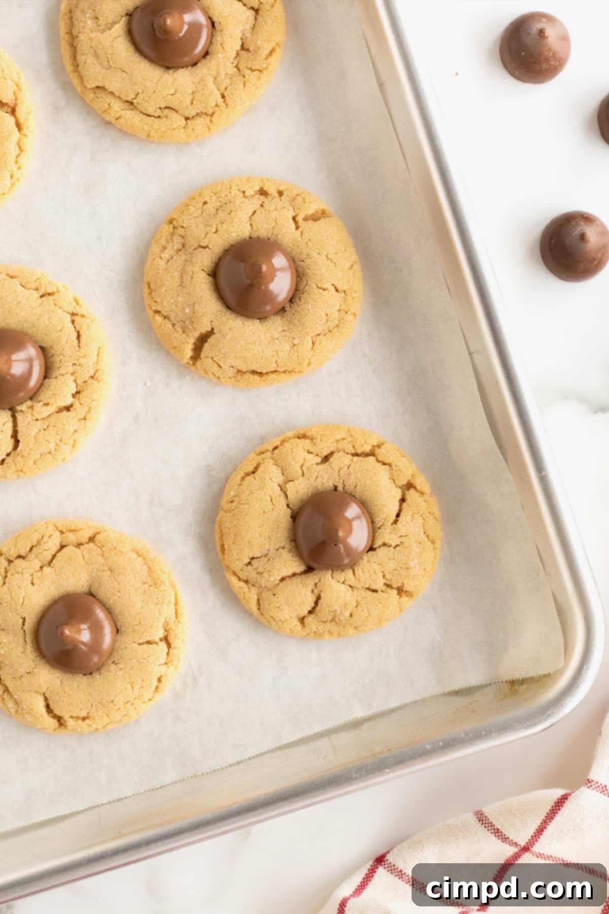 A parchment lined aluminum baking sheet with four peanut butter kiss cookies.