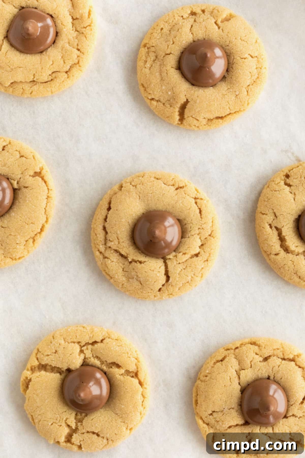 Four peanut butter kiss cookies on a parchment lined aluminum baking sheet.