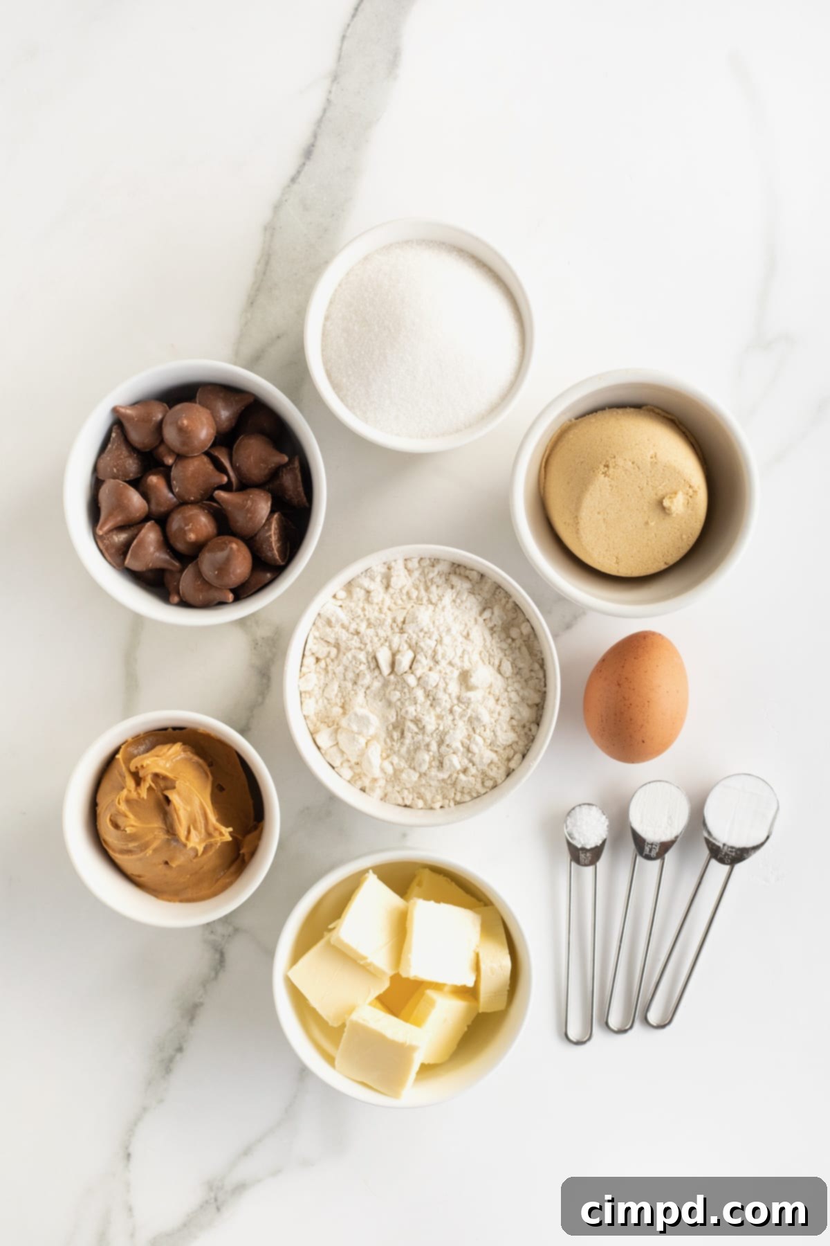 The ingredients to make peanut butter kiss cookies in small white glass dishes on a white counter.