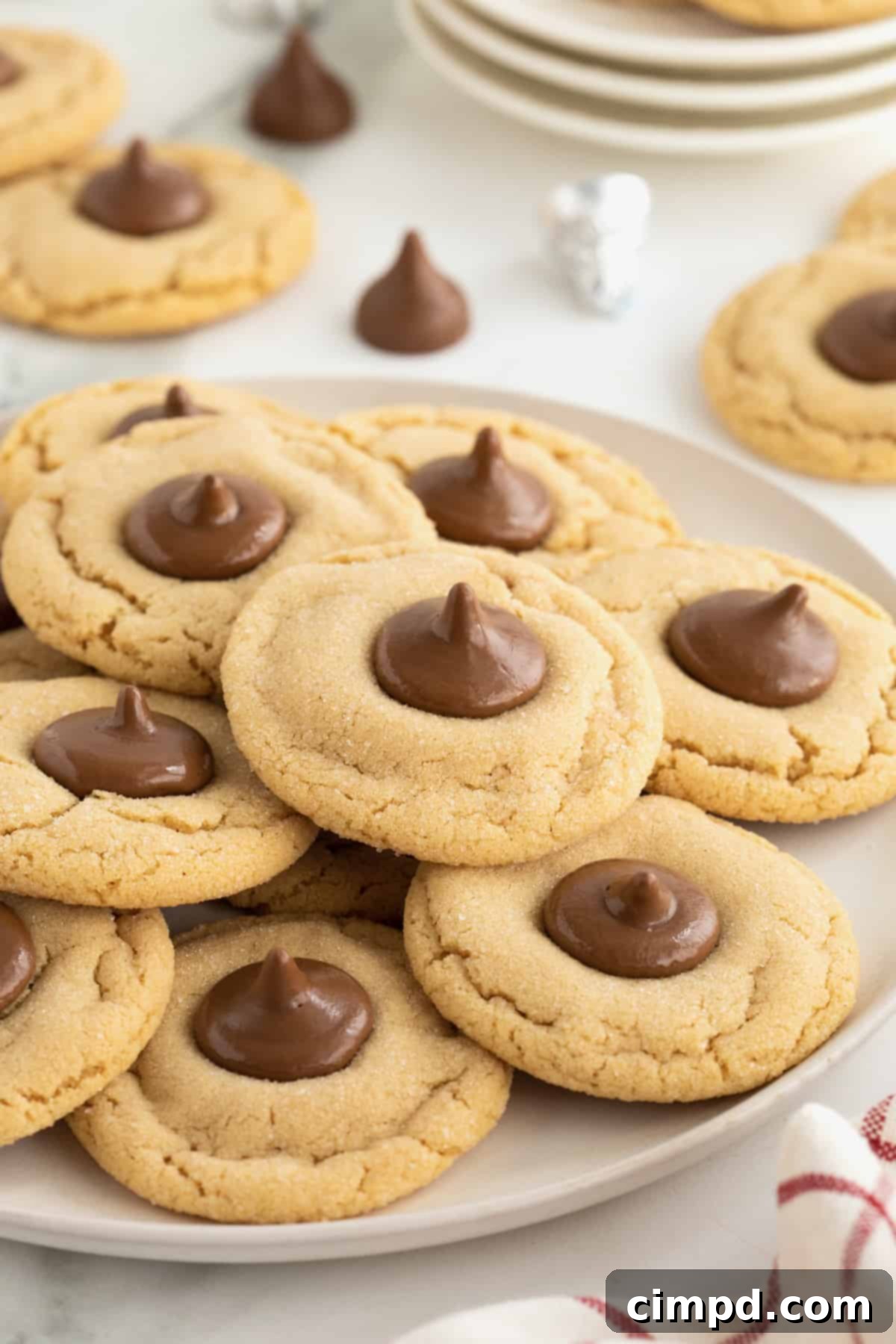 A pile of peanut butter holiday cookies with a Hershey's kiss in the center on a round white serving plate.