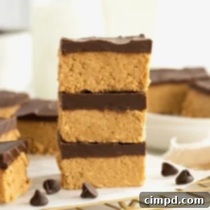 No Bake Peanut Butter Chocolate Bliss 10 Three chocolate peanut butter bars stacked on a parchment lined brass cooling rack with chocolate chips scattered around them.