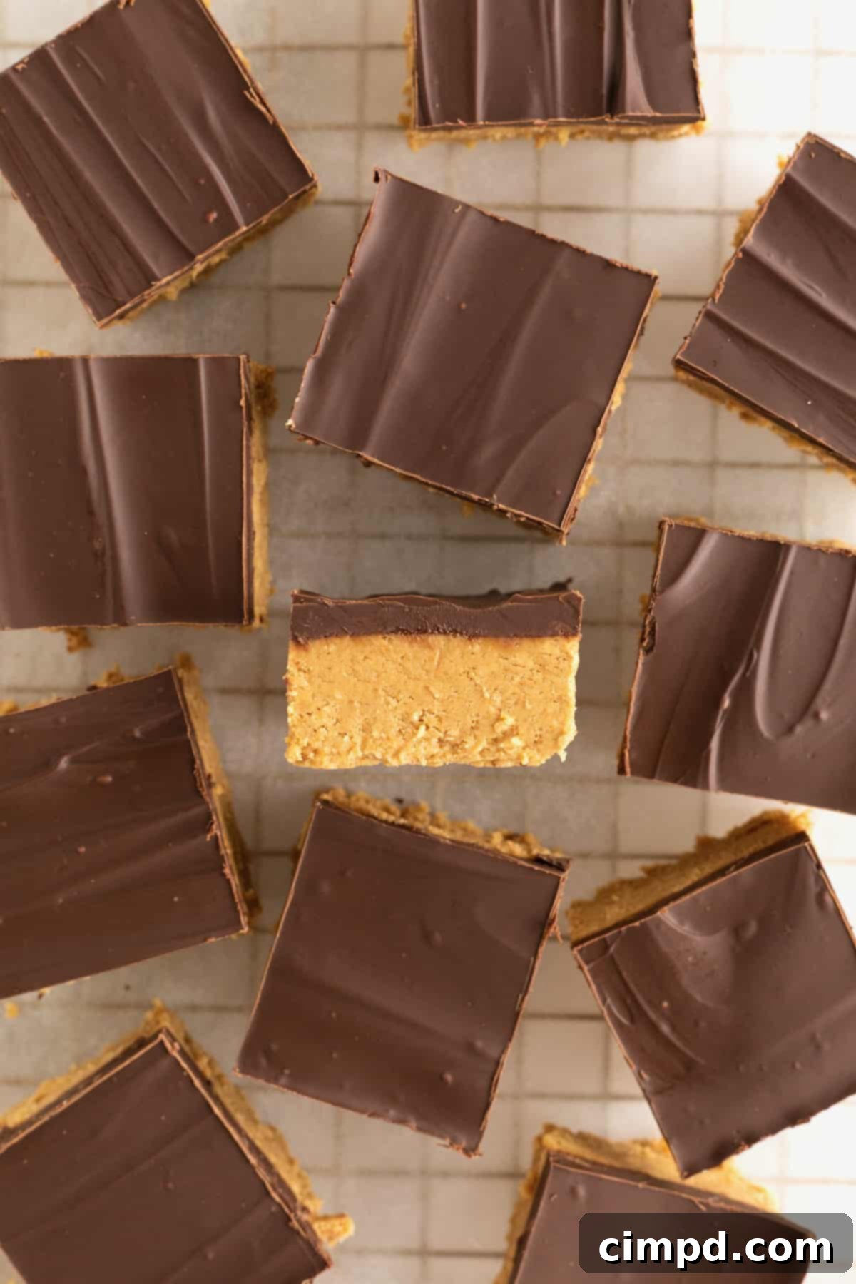 No Bake Peanut Butter Chocolate Bliss 9 Chocolate covered peanut butter bars cut into squares scattered on a parchment lined cooling rack. One square is turned on its side revealing the two layers.