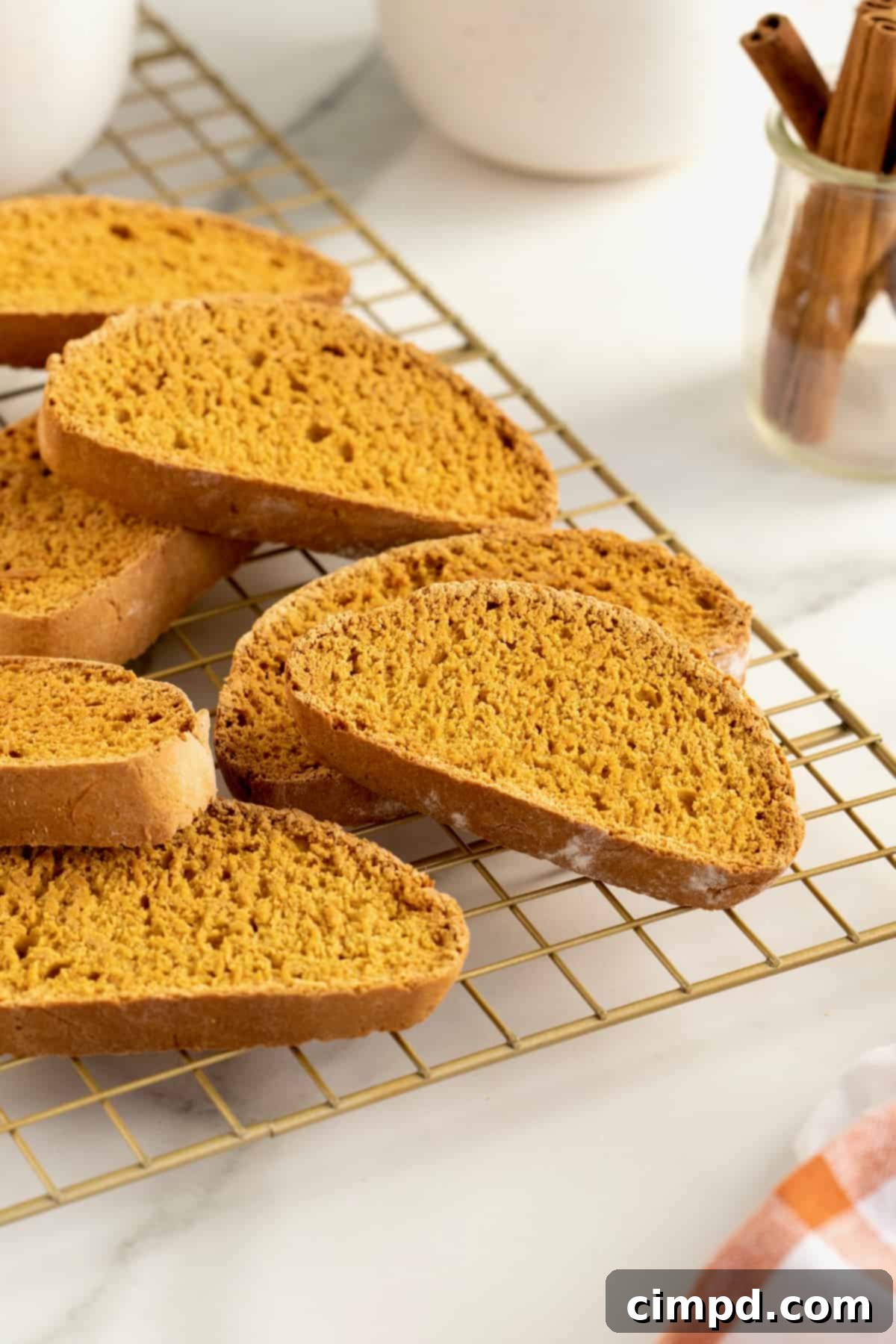 A stack of golden-orange pumpkin spice biscotti on a metal cooling rack, perfectly baked and ready to enjoy.