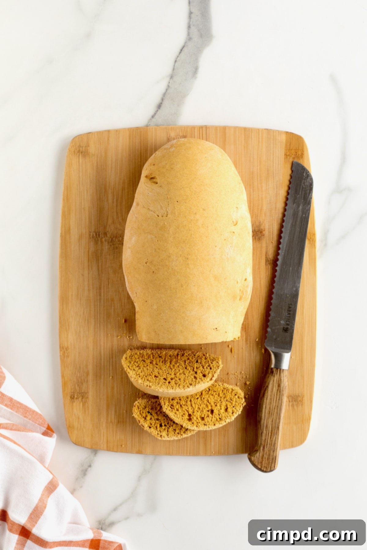 A perfectly baked loaf of biscotti rests on a light-colored wood cutting board, with a serrated knife poised to slice it.