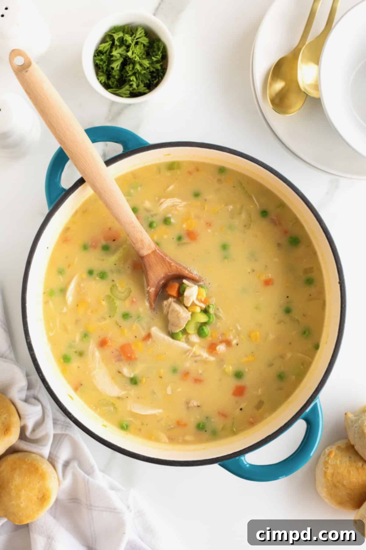 A stunning blue Dutch oven, artfully filled with luscious, creamy Chicken Pot Pie Soup, with a sturdy wooden spoon standing upright, suggesting its readiness to serve.
